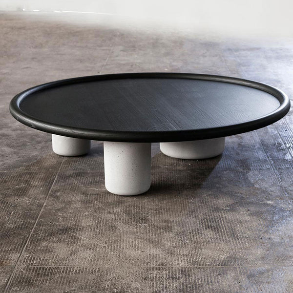Round black coffee table with a smooth top and textured white cylindrical legs, set against a neutral floor.