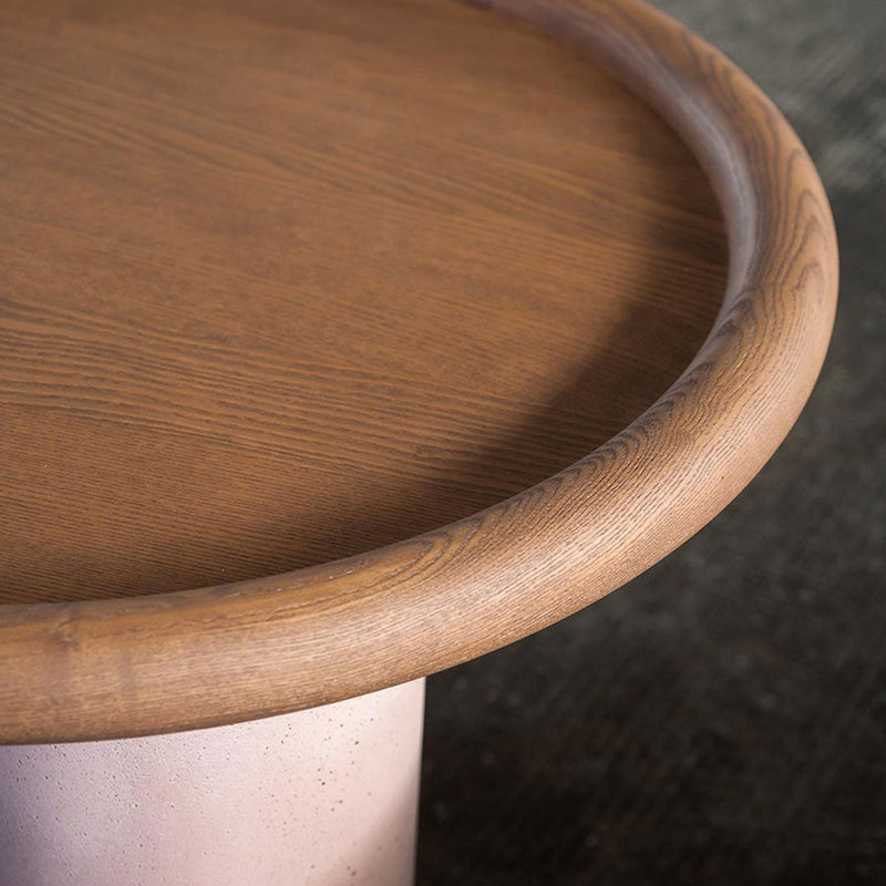 Wooden tabletop with a warm brown finish and a smooth round edge, set on a soft pink base.