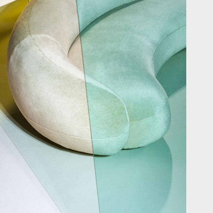 Curved sofa in soft beige and mint green, featuring smooth, velvety textures and a minimalist design.