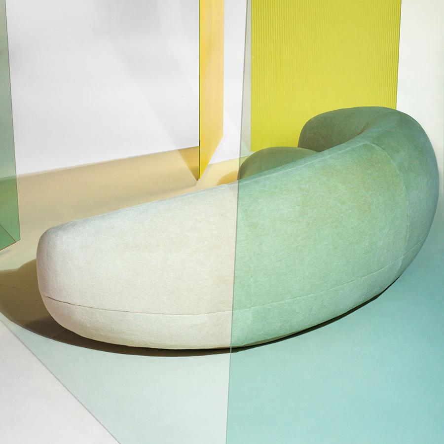 Curved sofa in soft cream and mint green hues, set against vibrant yellow and teal geometric backgrounds.