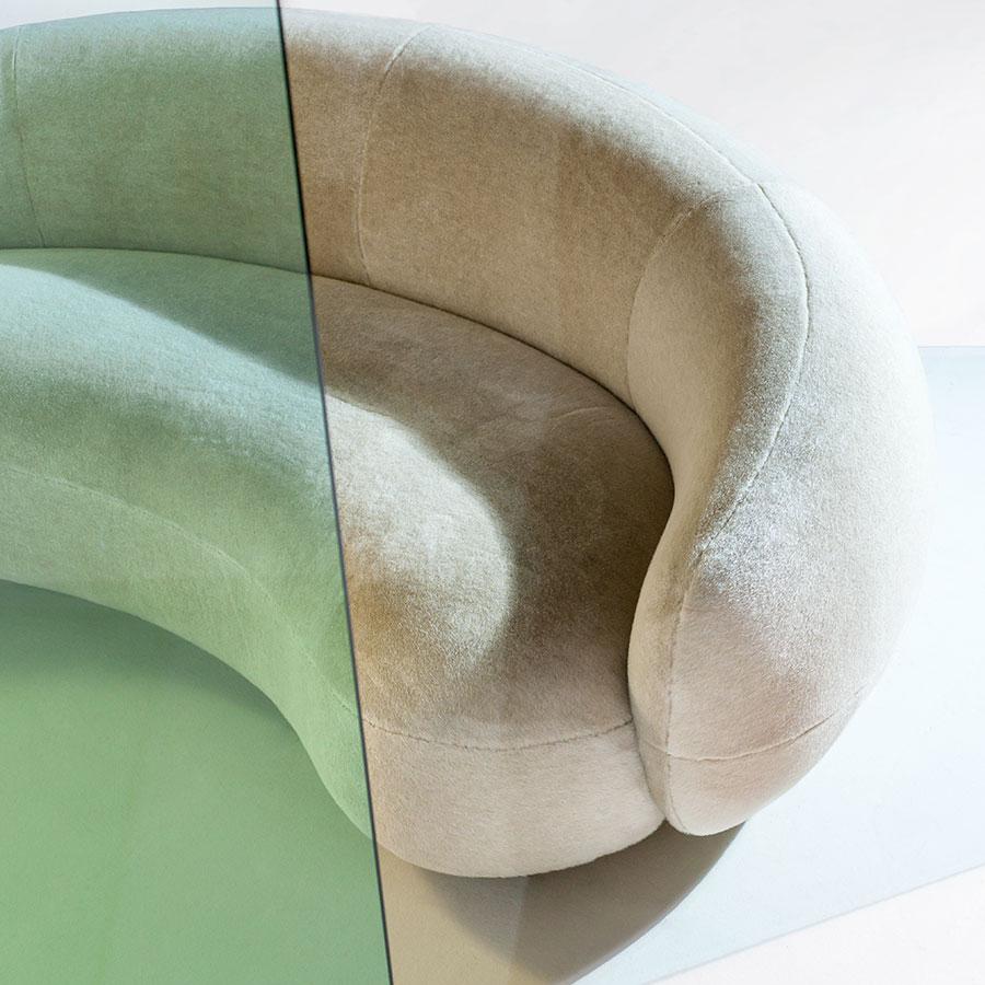 Curved sofa in soft beige velvet, featuring a contrasting green glass surface. Elegant, modern design with smooth lines.