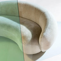 Curved sofa in soft beige velvet, featuring a contrasting green glass surface. Elegant, modern design with smooth lines.