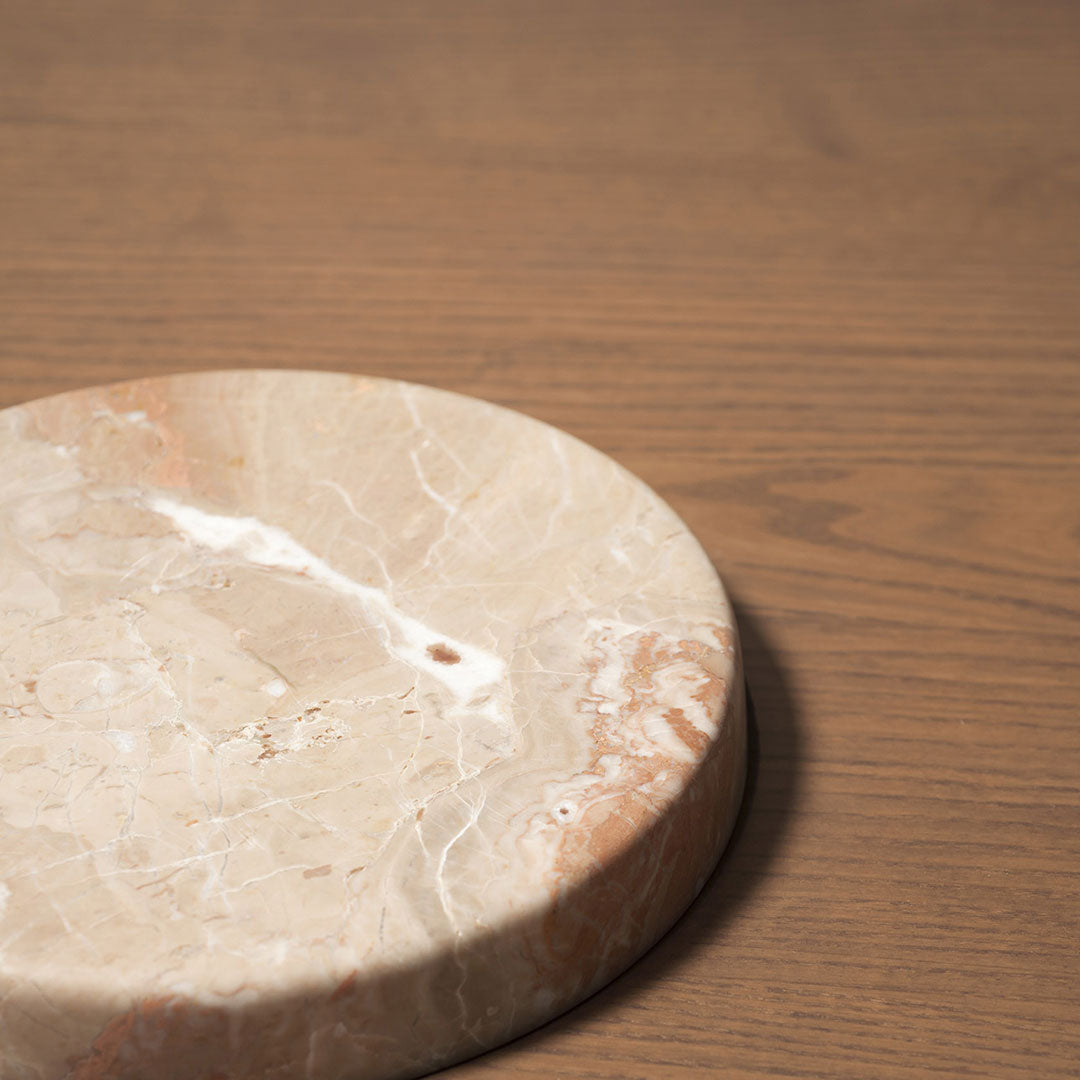 Beige and pink marble round tray with subtle veining on a wooden background. Elegant and modern design.