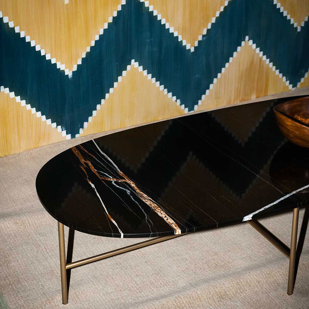 Sleek black marble coffee table with white and gold veining, set against a yellow and teal zigzag patterned wall.