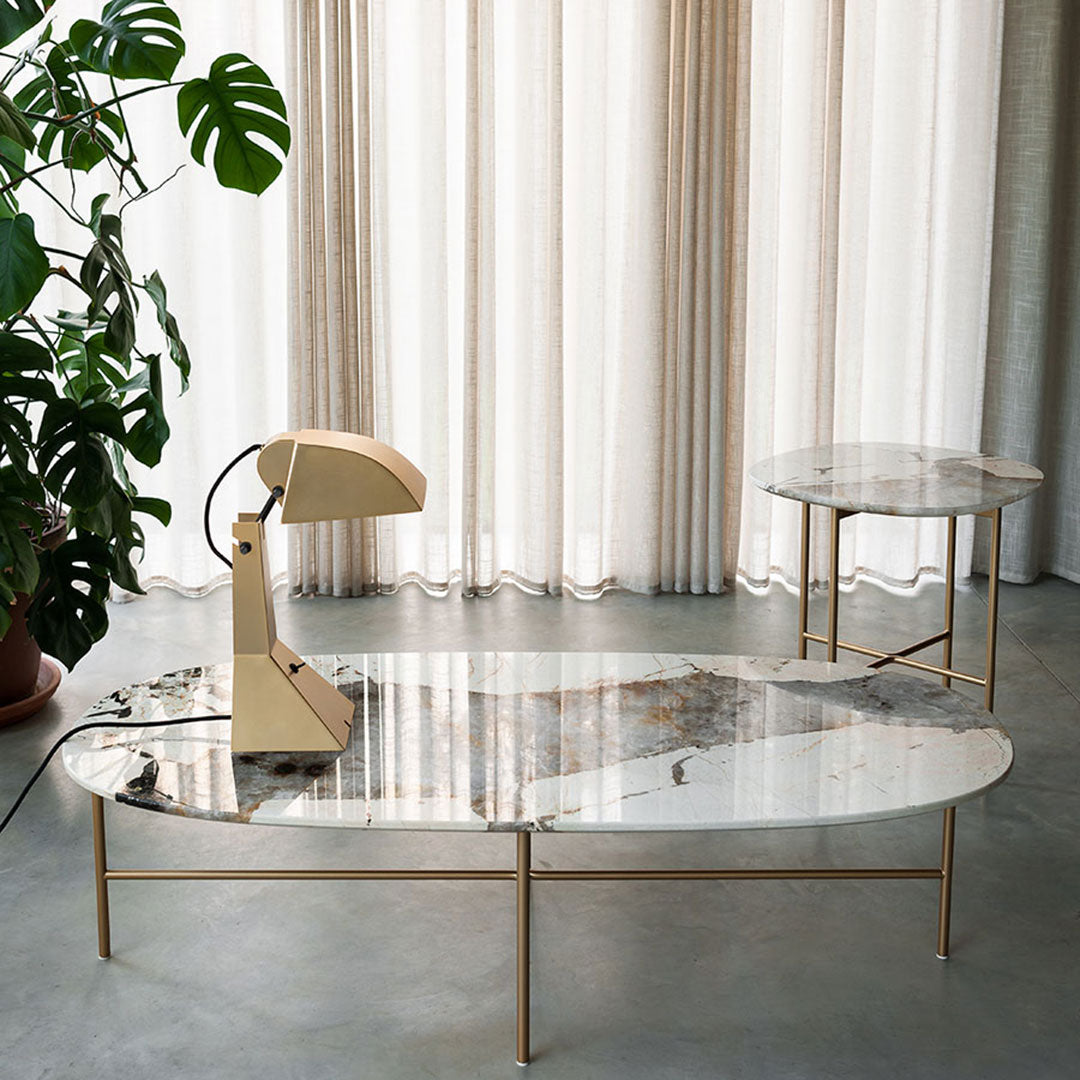 Elegant oval coffee table with a marble top featuring earthy tones and gold accents, set against neutral curtains.