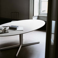 Sleek white oval table with a minimalist design, complemented by natural light and a neutral backdrop.