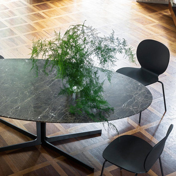 Oval black marble dining table with subtle gray veining, surrounded by sleek black chairs on a warm wooden floor.