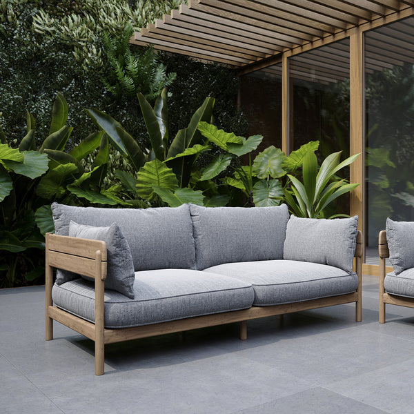 Gray outdoor sofa with plush cushions and wooden frame, surrounded by lush green foliage. Ideal for modern patios.