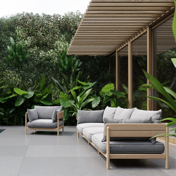 Modern outdoor sofa set featuring gray cushions with light wood frames, against lush green foliage backdrop.
