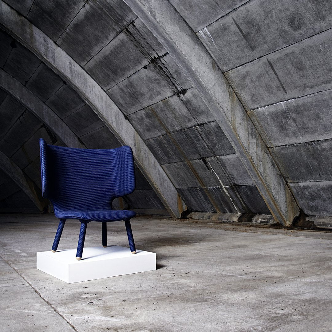 Navy blue upholstered chair with a minimalist design, set on a white base against a textured concrete backdrop.