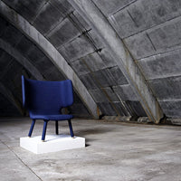 Navy blue upholstered chair with a minimalist design, set on a white base against a textured concrete backdrop.