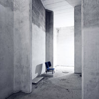 Minimalist design featuring a blue chair in a stark, concrete space with gray walls and soft shadows.