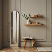 Full-length mirror with sleek design, set against a beige wall, featuring natural wood shelves and a warm wooden floor pattern.