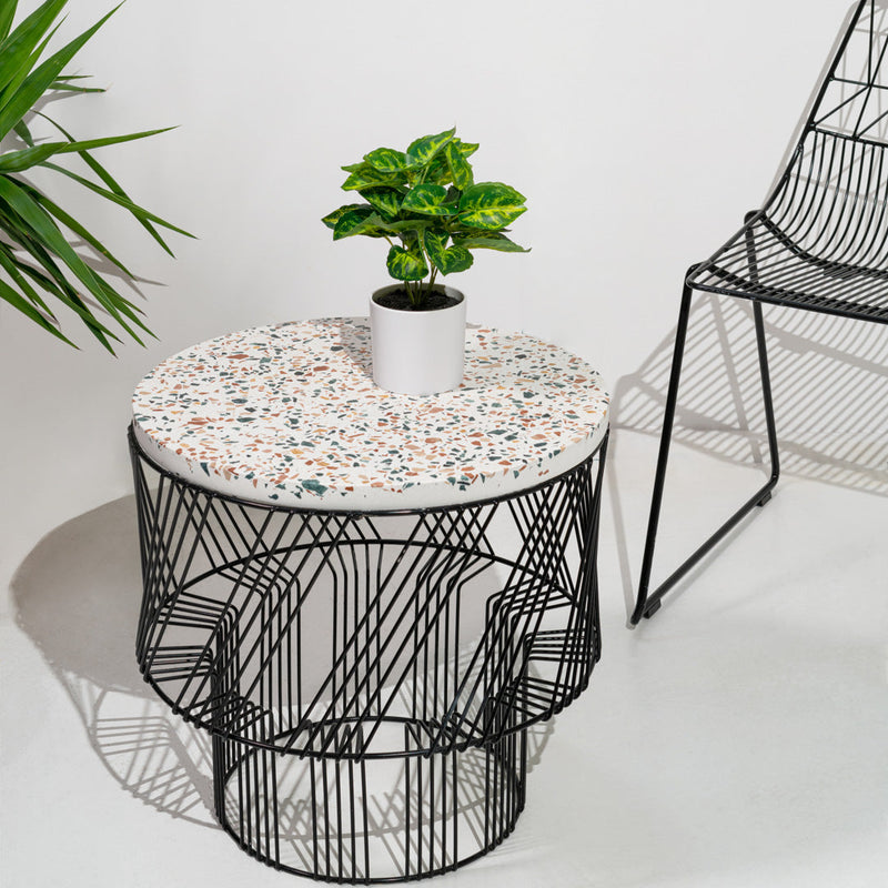 Round table with a speckled white top, black wire base, and a small green plant in a white pot. Modern and stylish design.