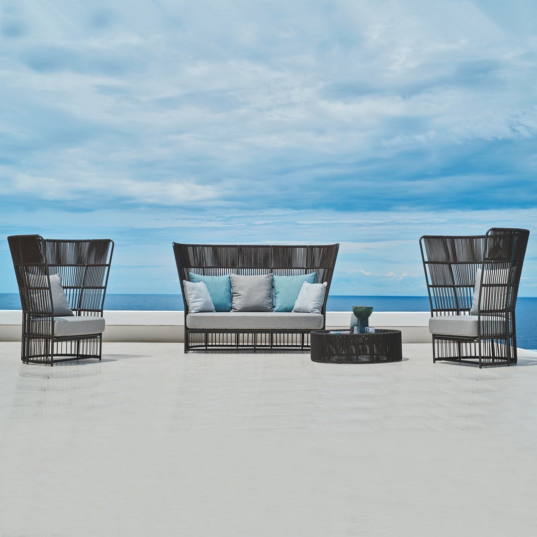 "Black woven patio furniture set with light blue cushions against a serene blue sky and ocean backdrop."