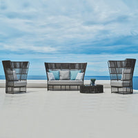 "Black woven patio furniture set with light blue cushions against a serene blue sky and ocean backdrop."