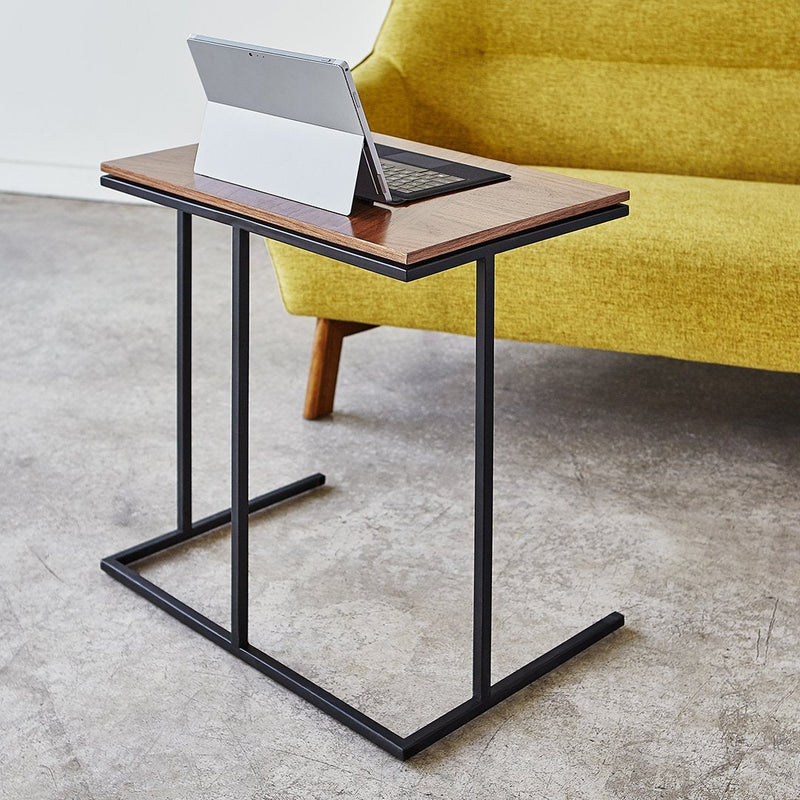 Brown wood-top side table with black metal frame, paired with a vibrant yellow sofa. Modern and stylish design.