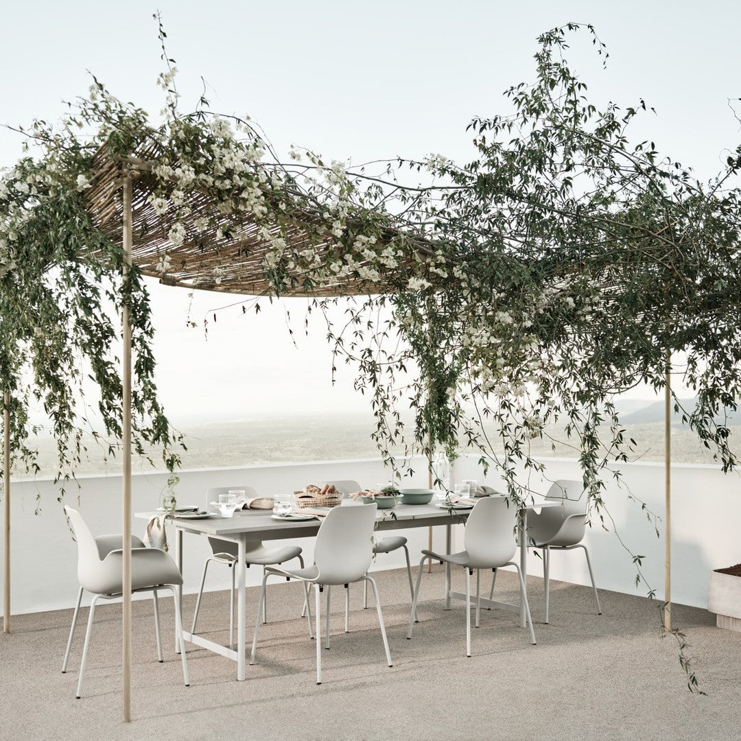 Elegant outdoor dining setup featuring white chairs and a natural woven canopy adorned with greenery and soft white blooms.