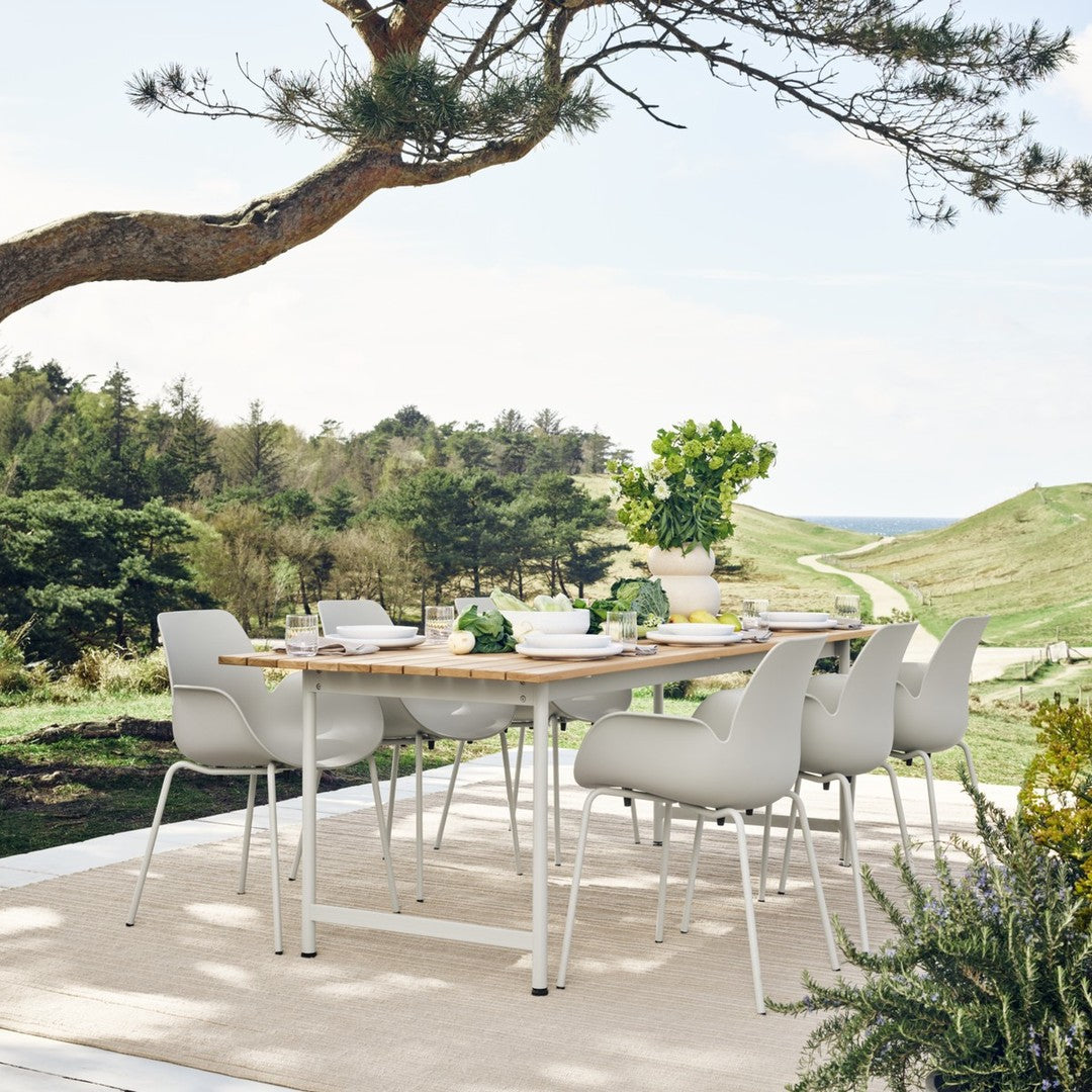 Modern white dining chairs around a wooden table, set against a green landscape and blue sky. Ideal for outdoor decor.