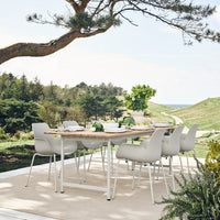 Modern white dining chairs around a wooden table, set against a green landscape and blue sky. Ideal for outdoor decor.