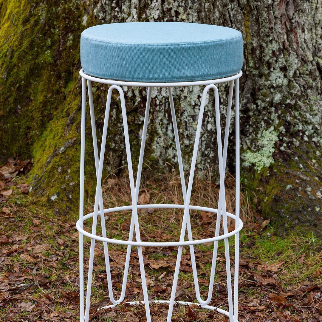 Light blue upholstered seat on a white geometric metal bar stool, set against a natural background.