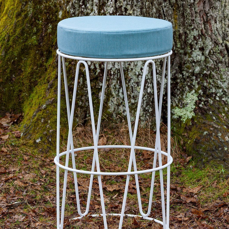 Light blue upholstered seat on a white geometric metal bar stool, set against a natural background.