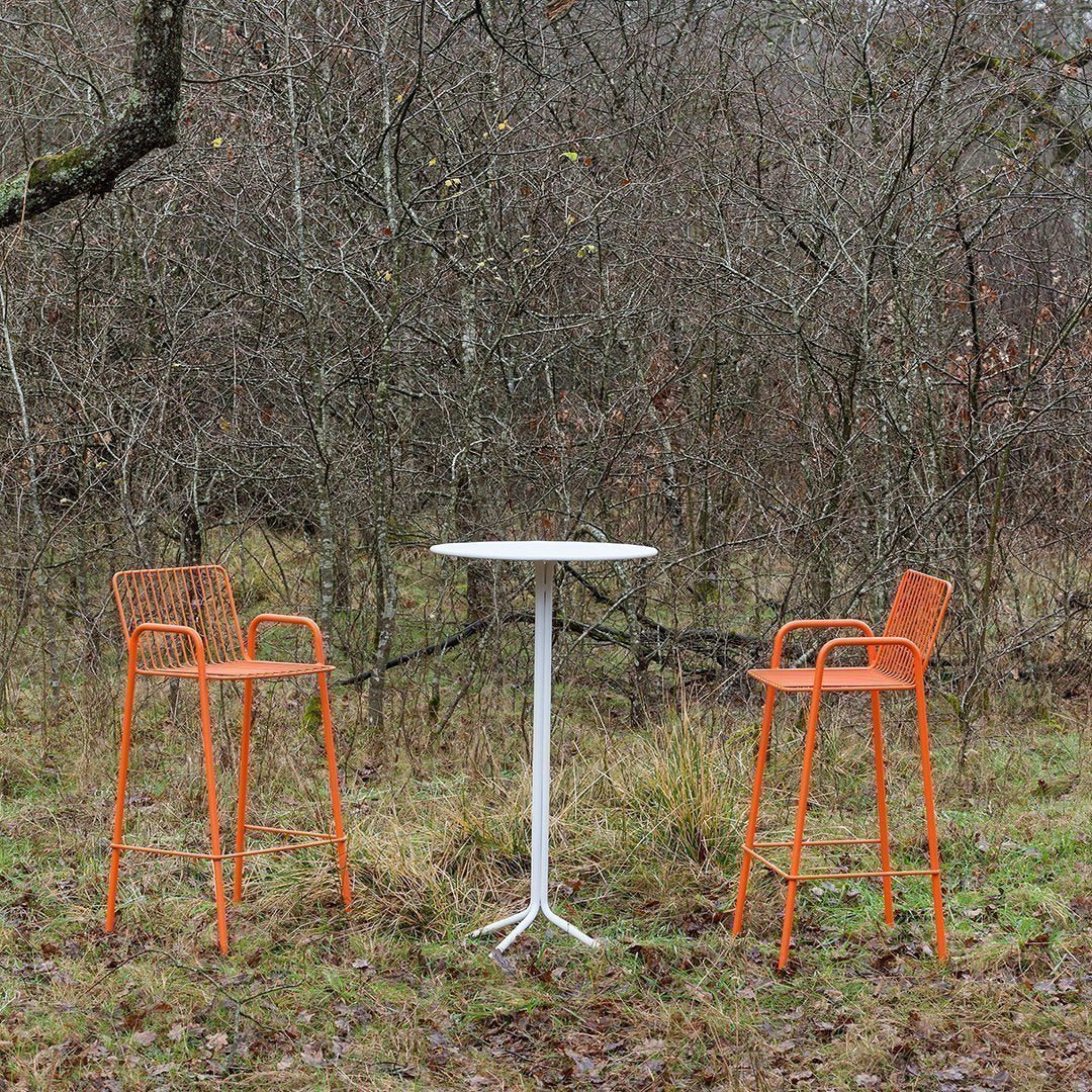 Orange bar stools and white round table set against a natural backdrop. Modern design with a sleek finish.