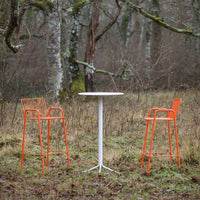 "Set of two vibrant orange bar stools and a sleek white table against a natural backdrop."