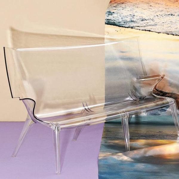 Clear acrylic bench with sleek lines, set against pastel and ocean-inspired background colors and soft textures.
