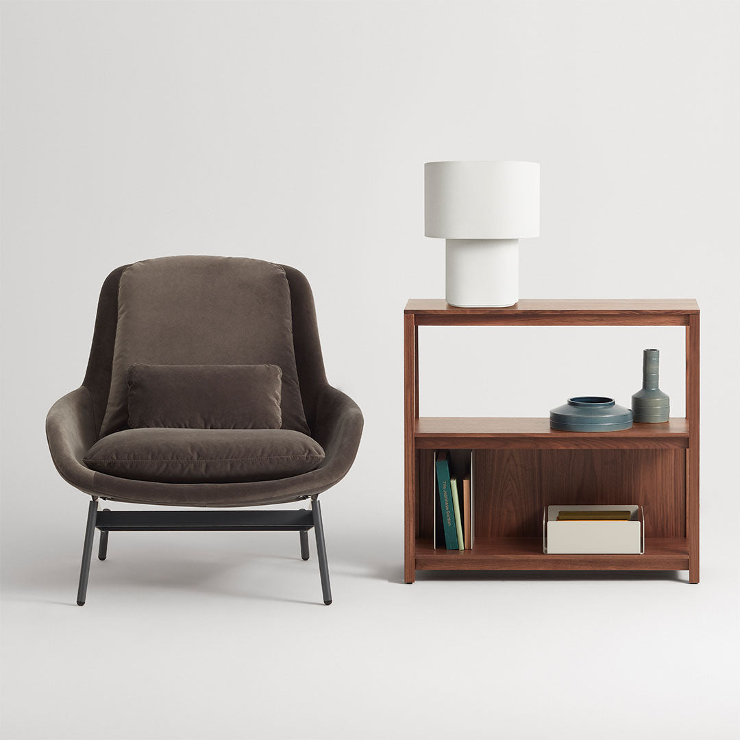 Modern brown upholstered chair with sleek black legs beside a wooden shelf, featuring neutral tones and minimalist design.