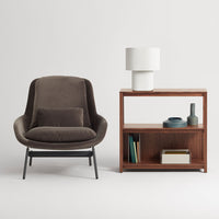 Modern brown upholstered chair with sleek black legs beside a wooden shelf, featuring neutral tones and minimalist design.