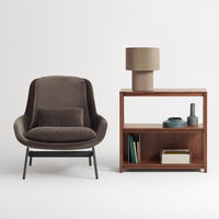 Brown velvet chair with black metal legs, paired with a wooden shelf. Soft beige lamp complements the warm color palette.