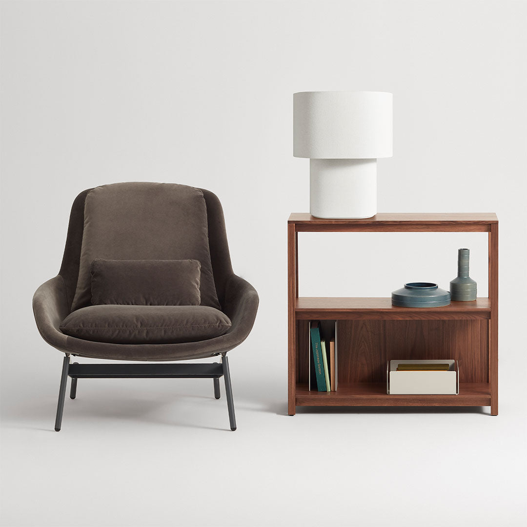Brown upholstered chair with a smooth texture, paired with a wooden bookshelf and white lamp, featuring clean lines.
