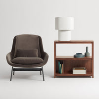 Brown upholstered chair with a smooth texture, paired with a wooden bookshelf and white lamp, featuring clean lines.