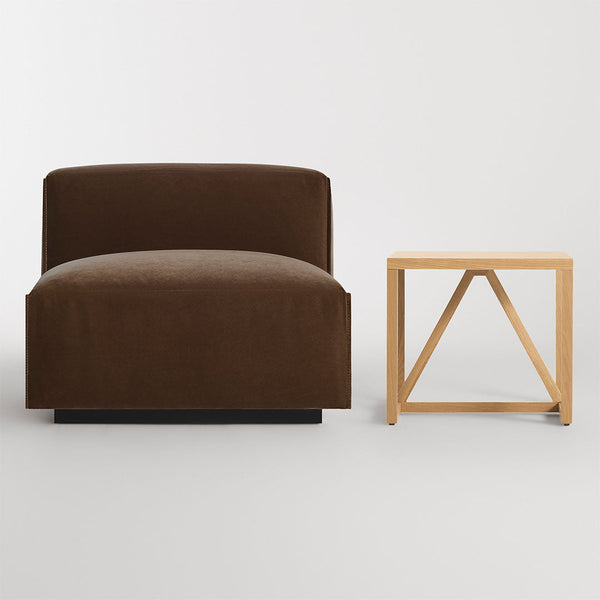 Brown velvet chair with a simple, solid design next to a natural wood side table featuring an angular base.