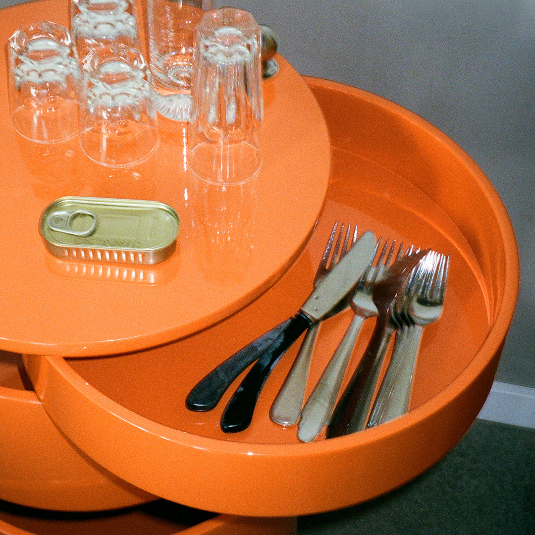 Bright orange serving tray with glossy finish, featuring black and metallic silver cutlery and clear glassware.