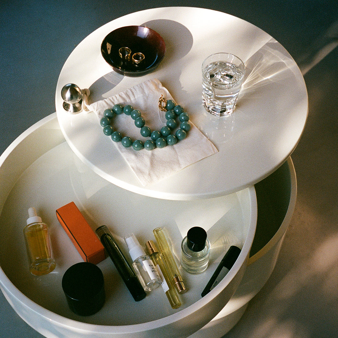 "White circular trays with a mix of textured items, including turquoise jewelry, glass, and colorful cosmetic bottles."
