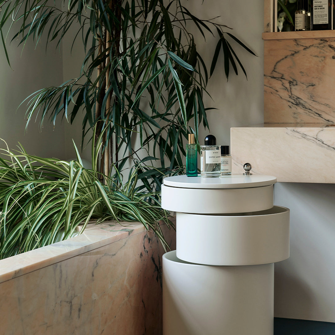 Modern white cylindrical side tables with a smooth finish, set against natural green foliage and marble textures.