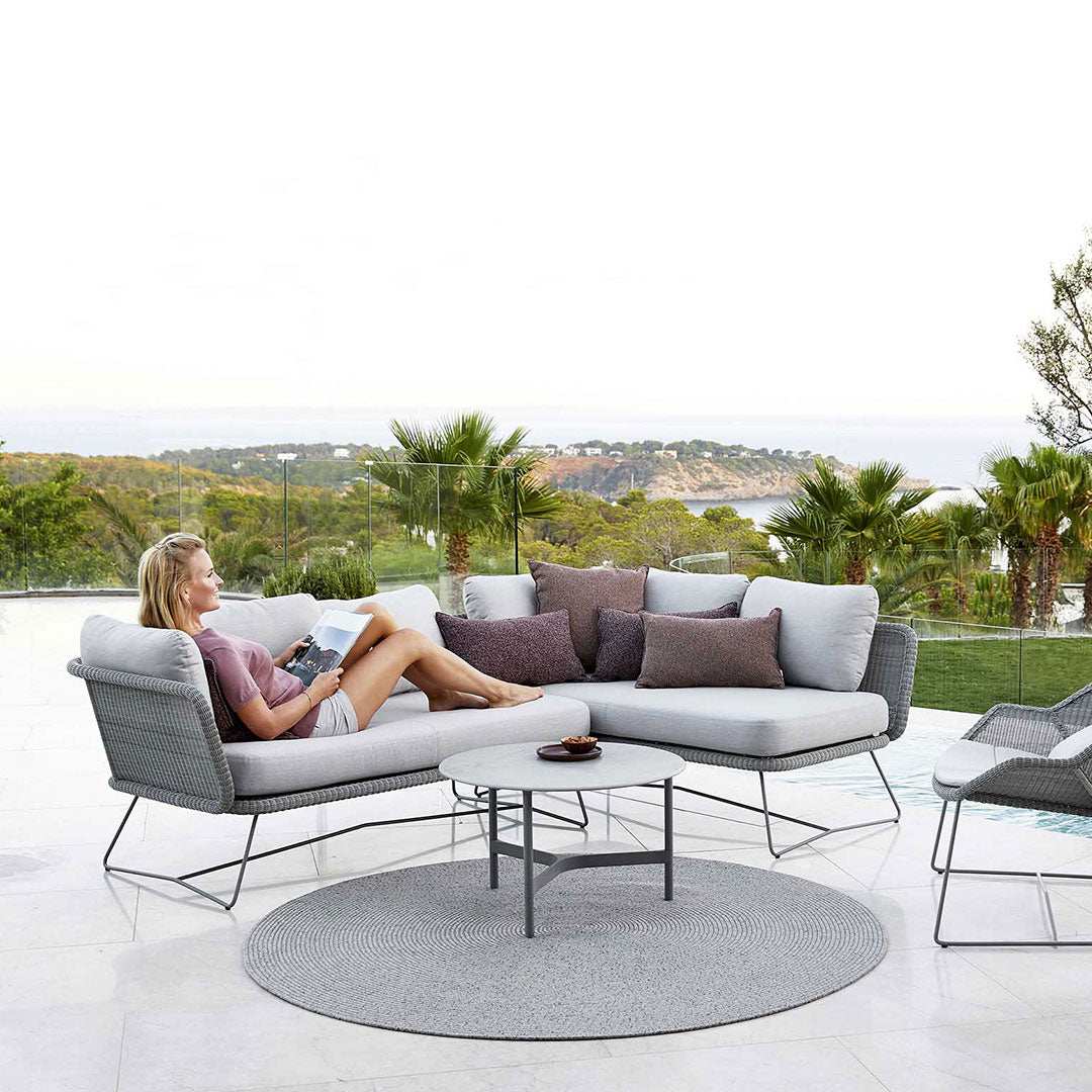 "Modern outdoor sectional sofa in gray tones with mixed patterned cushions, featuring a round gray rug."