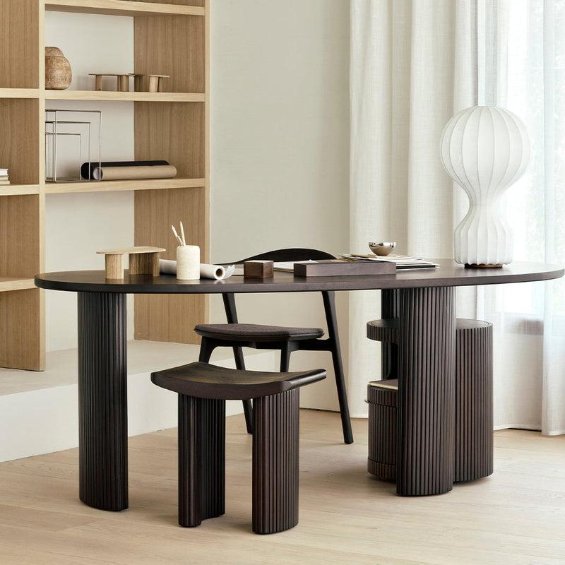 Elegant dark wood dining table with curved edges, paired with matching stools, set against a light, neutral backdrop.