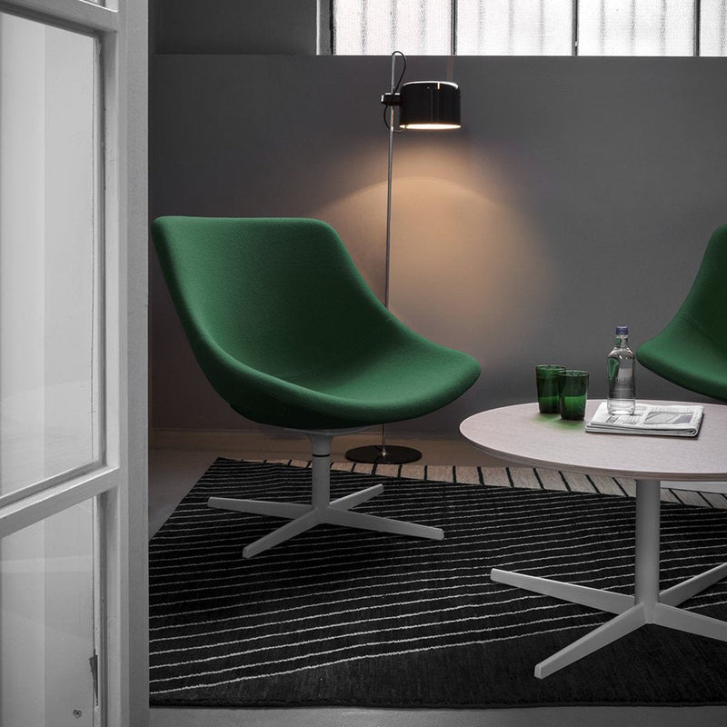 Green swivel chairs on a striped black and white rug with a round light wood table and green glassware.