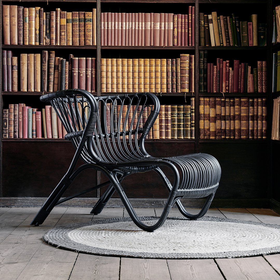 Modern black rattan chair with curved lines, set against a backdrop of colorful vintage books in a cozy library.