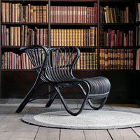 Modern black rattan chair with curved lines, set against a backdrop of colorful vintage books in a cozy library.