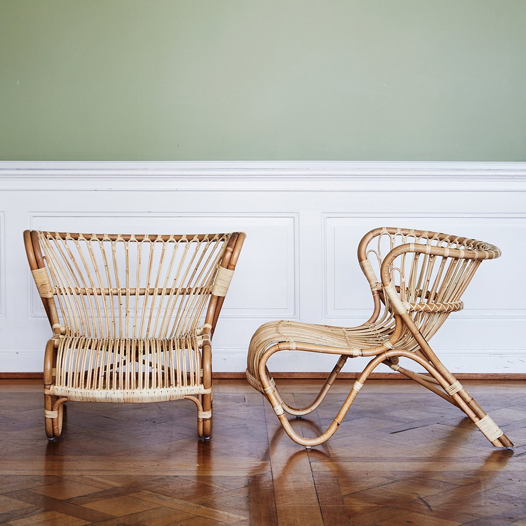 Natural rattan chairs with smooth curves and intricate woven patterns against a soft green wall.