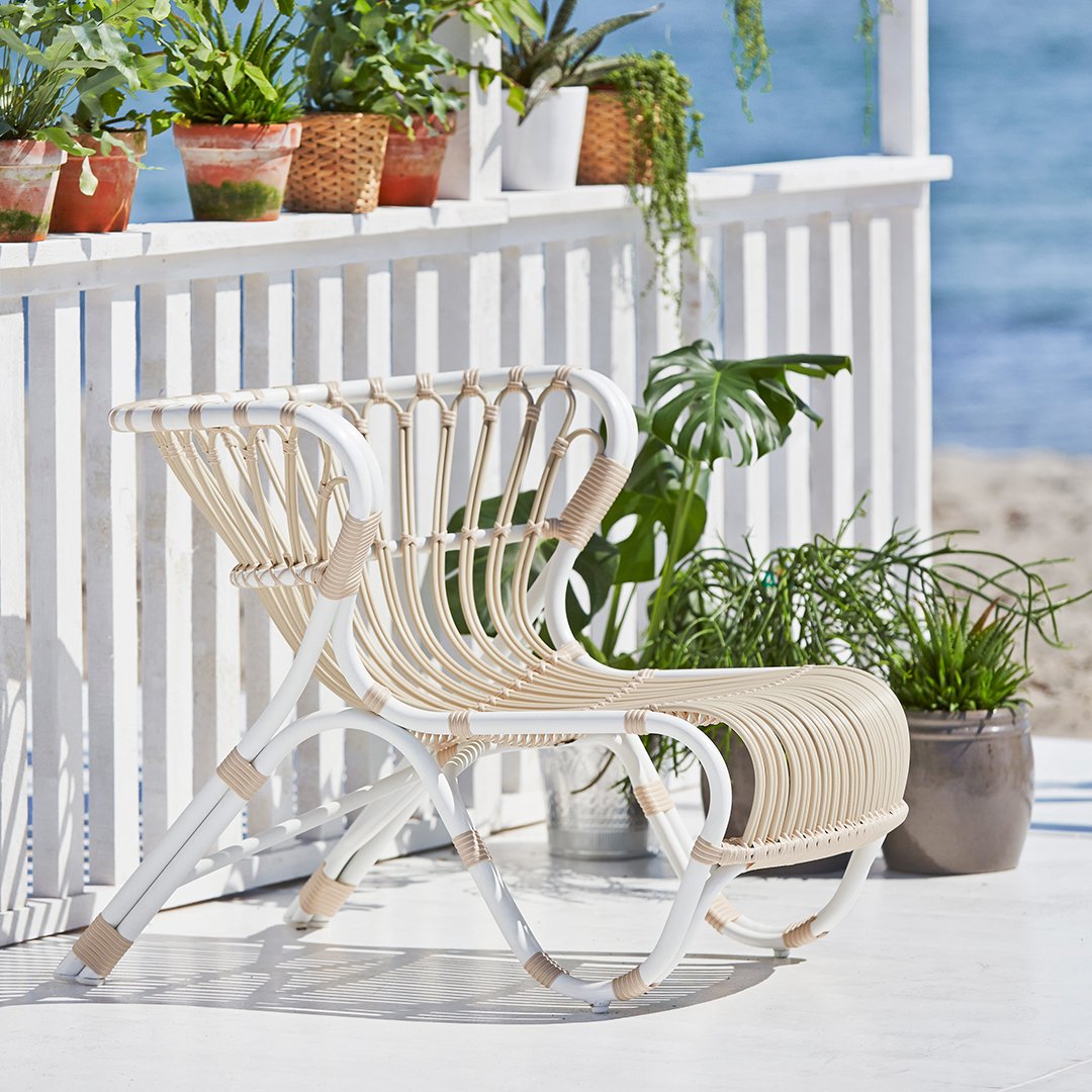 White and beige slatted lounge chair with a modern design, set against a beachside backdrop and greenery.