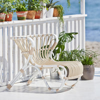 White and beige slatted lounge chair with a modern design, set against a beachside backdrop and greenery.