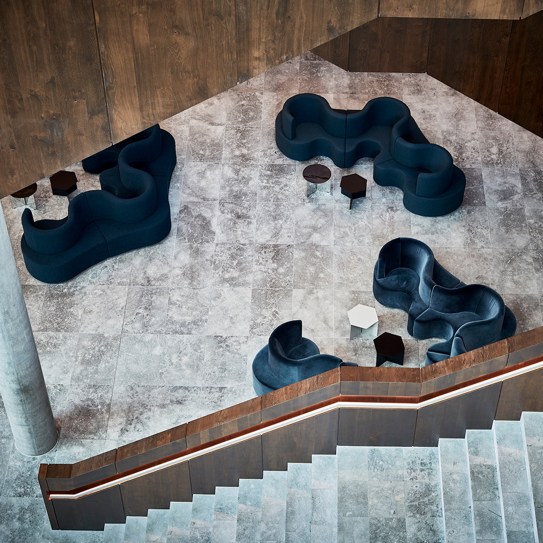 Modern seating in deep blue upholstery on a light gray stone floor, featuring smooth, flowing shapes and dark accent tables.