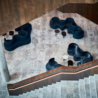 Modern seating in deep blue upholstery on a light gray stone floor, featuring smooth, flowing shapes and dark accent tables.