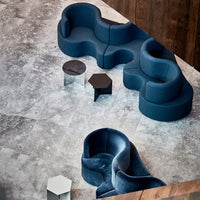 Modern dark blue sofa with smooth curves, complemented by sleek black and clear accent tables on a textured gray floor.