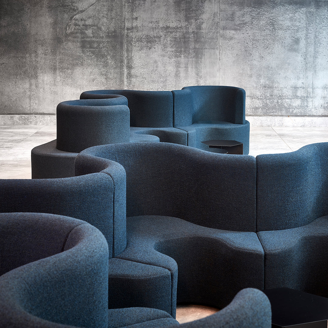 Curved, modular seating in deep navy blue fabric against a textured gray concrete background. Stylish and modern design.